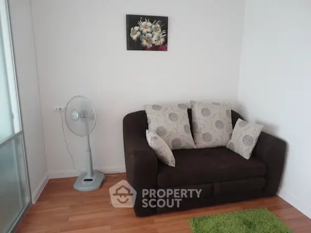 Cozy living room with a dark sofa, decorative pillows, and a fan, perfect for relaxation.