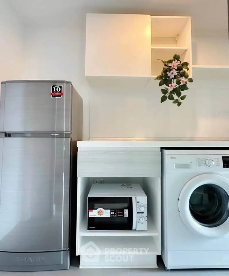 Modern kitchen with sleek appliances including fridge, microwave, and washing machine in a stylish setup.