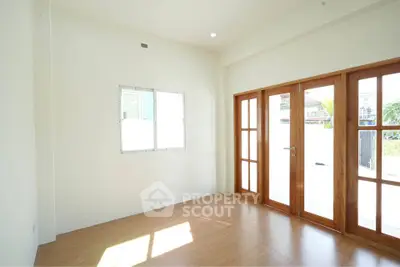 Bright empty room with wooden floor and large glass doors leading to outdoor space.