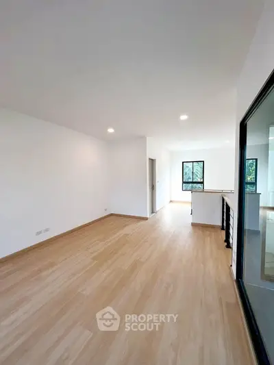 Spacious open-plan living room with wooden flooring and large windows for natural light.