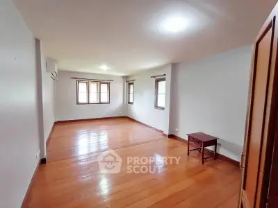Spacious empty room with wooden flooring and natural light from multiple windows.