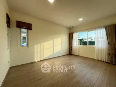 Spacious sunlit room with wooden flooring and large windows, perfect for a cozy living space.