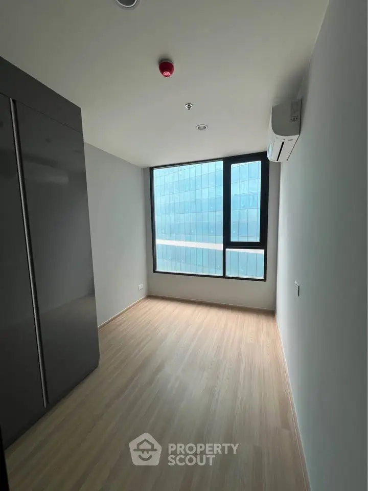 Modern minimalist bedroom with large window and sleek wardrobe in high-rise apartment.
