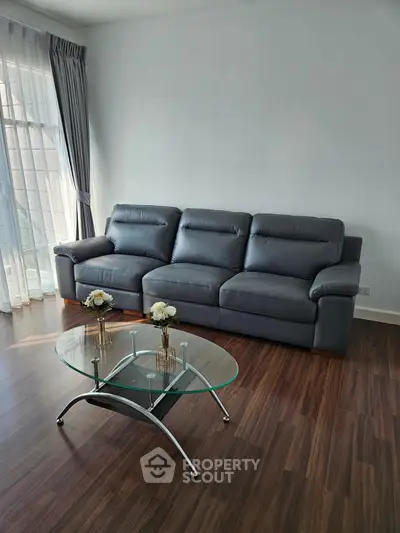 Modern living room with sleek leather sofa and glass coffee table, featuring elegant wooden flooring.