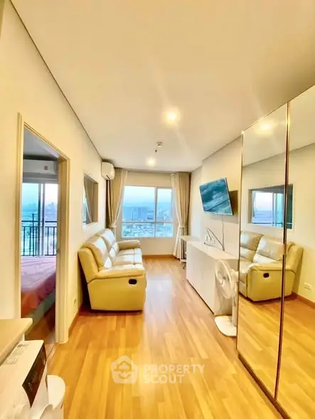 Modern living room with city view, featuring sleek furniture and large mirror for spacious feel.