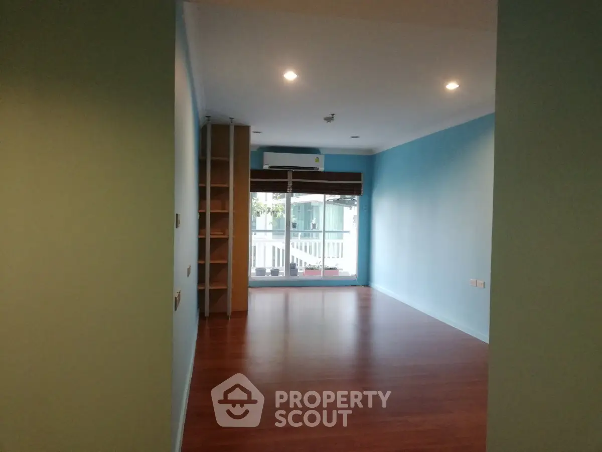 Spacious empty room with wooden flooring and large window, ideal for customization.
