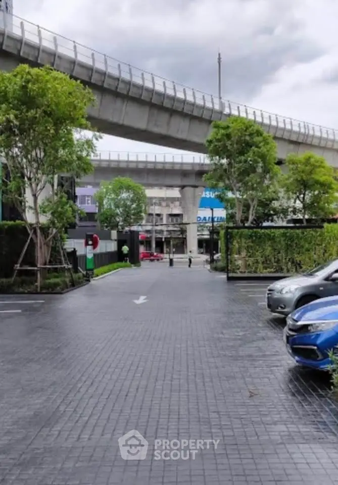 Modern urban parking area with lush greenery and elevated railway view.
