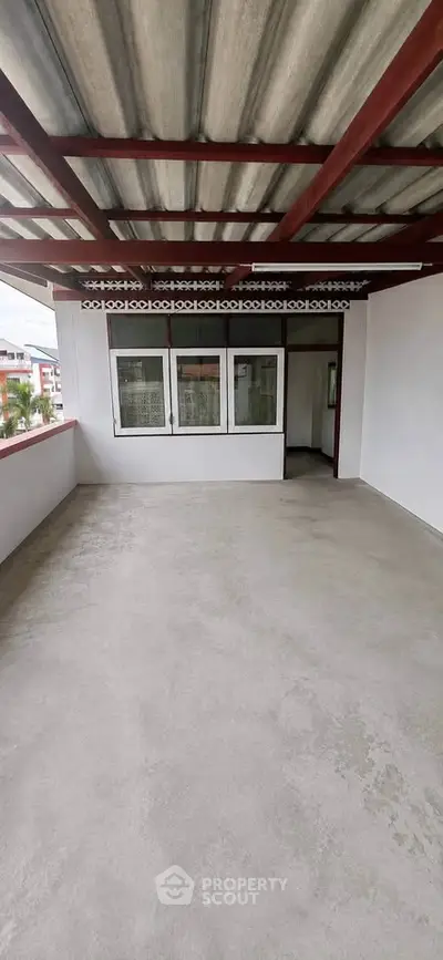 Spacious covered balcony with concrete flooring and red metal roof, ideal for outdoor relaxation.