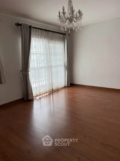 Spacious empty room with elegant chandelier and large window, perfect for customization.
