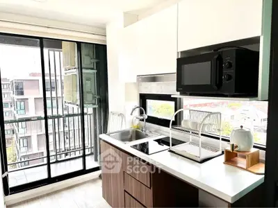 Modern kitchen with sleek cabinetry and balcony view, featuring a microwave and dish rack.