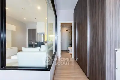 Modern apartment hallway with wooden flooring and glass partition, leading to a sleek bathroom.