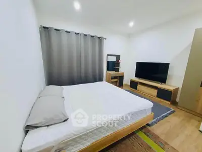 Modern bedroom with minimalist decor and large TV, featuring cozy lighting and wooden flooring.