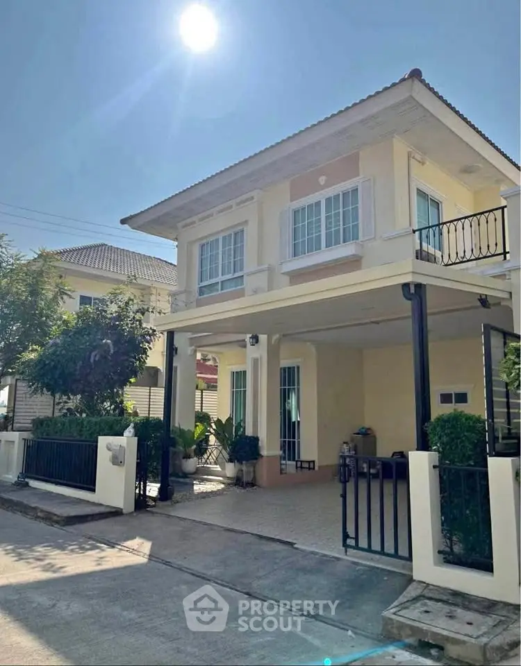 Charming two-story house with balcony and gated entrance under bright sunlight.
