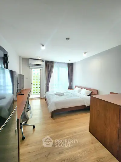 Spacious modern bedroom with large window and wooden flooring in a stylish apartment.