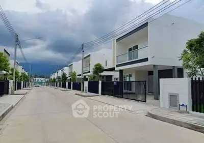 Modern residential street with contemporary white houses and lush greenery.