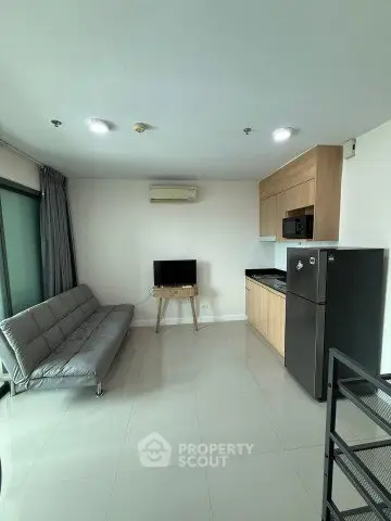 Modern living room with sleek furniture and compact kitchen area in a bright apartment.