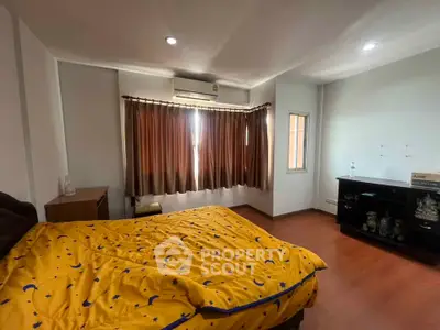 Spacious bedroom with wooden flooring and natural light, featuring a cozy bed and elegant curtains.