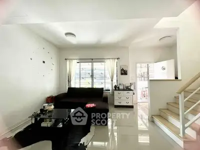 Bright living room with modern decor and staircase, featuring a cozy sofa and glass coffee table.