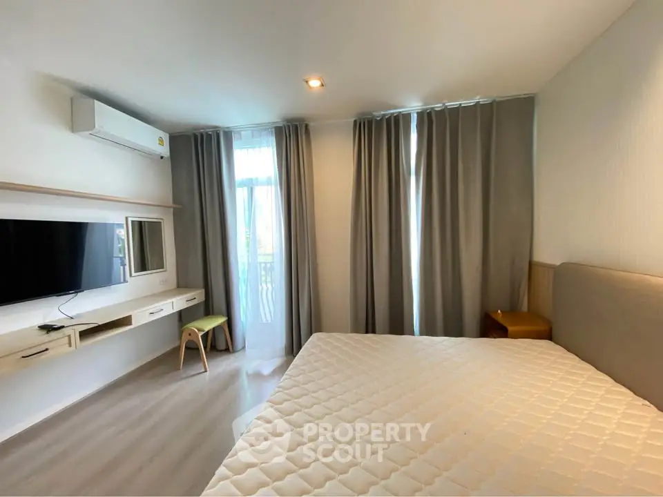 Modern bedroom with natural light, featuring a large bed, wall-mounted TV, and stylish decor.