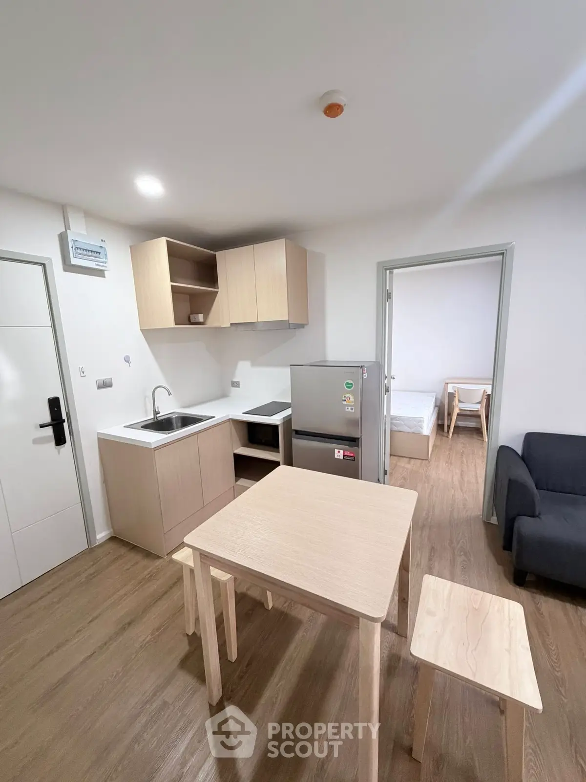 Modern compact kitchen with wooden cabinets and dining area in a cozy apartment setting.