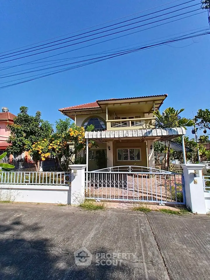 Charming two-story house with lush garden and gated entrance under clear blue sky.