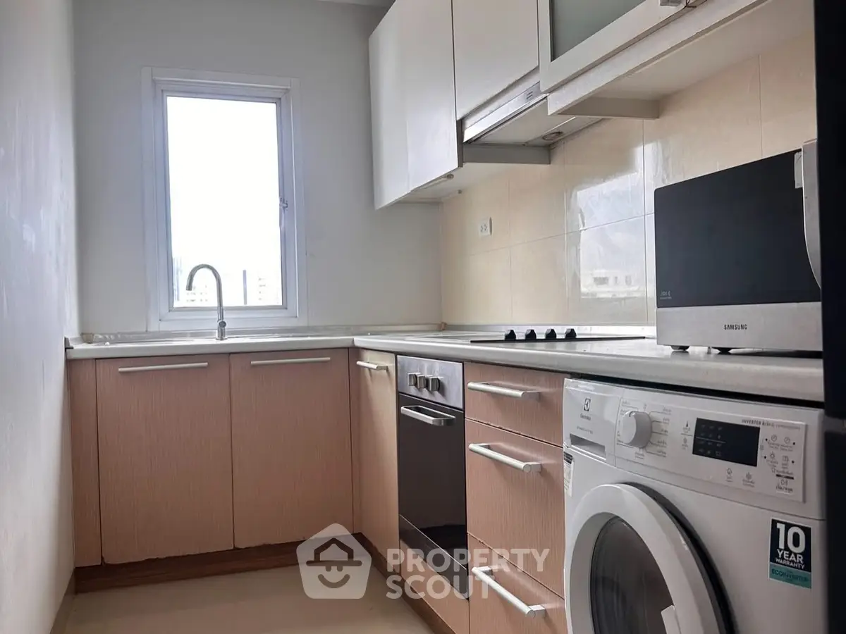 Modern kitchen with sleek appliances and natural light, featuring a washing machine and oven.