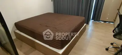 Modern bedroom with wooden flooring and brown bedspread, featuring a sleek chair and floor-to-ceiling curtains.
