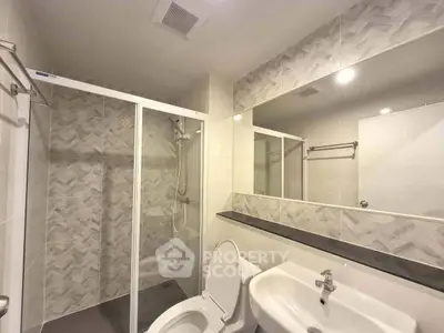 Modern bathroom with glass shower and large mirror in sleek apartment.