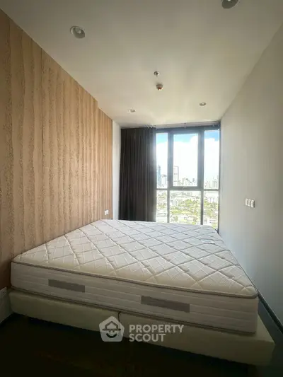 Spacious bedroom with large window offering stunning city views, featuring a comfortable mattress and modern decor.