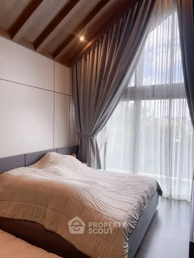 Luxurious bedroom with vaulted ceiling and large window draped in elegant curtains.