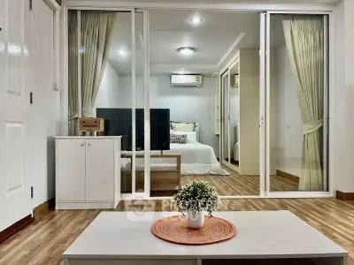 Modern living room with sliding glass doors leading to a cozy bedroom, featuring stylish decor and wooden flooring.