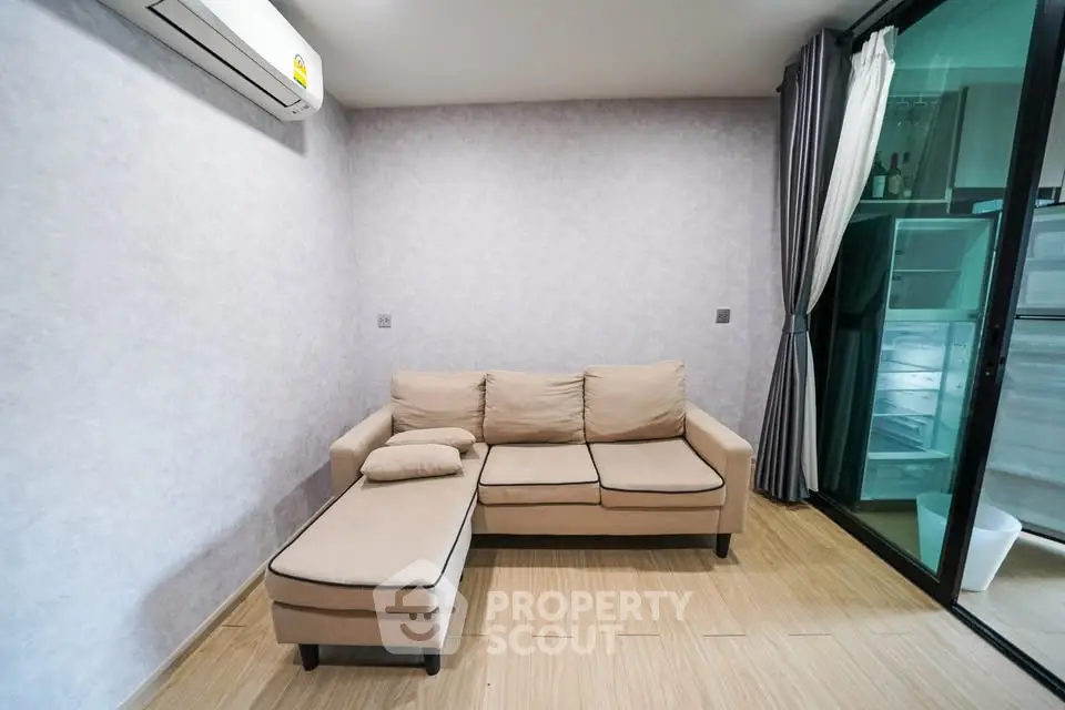 Modern living room with beige sectional sofa and air conditioning, featuring sliding glass doors.