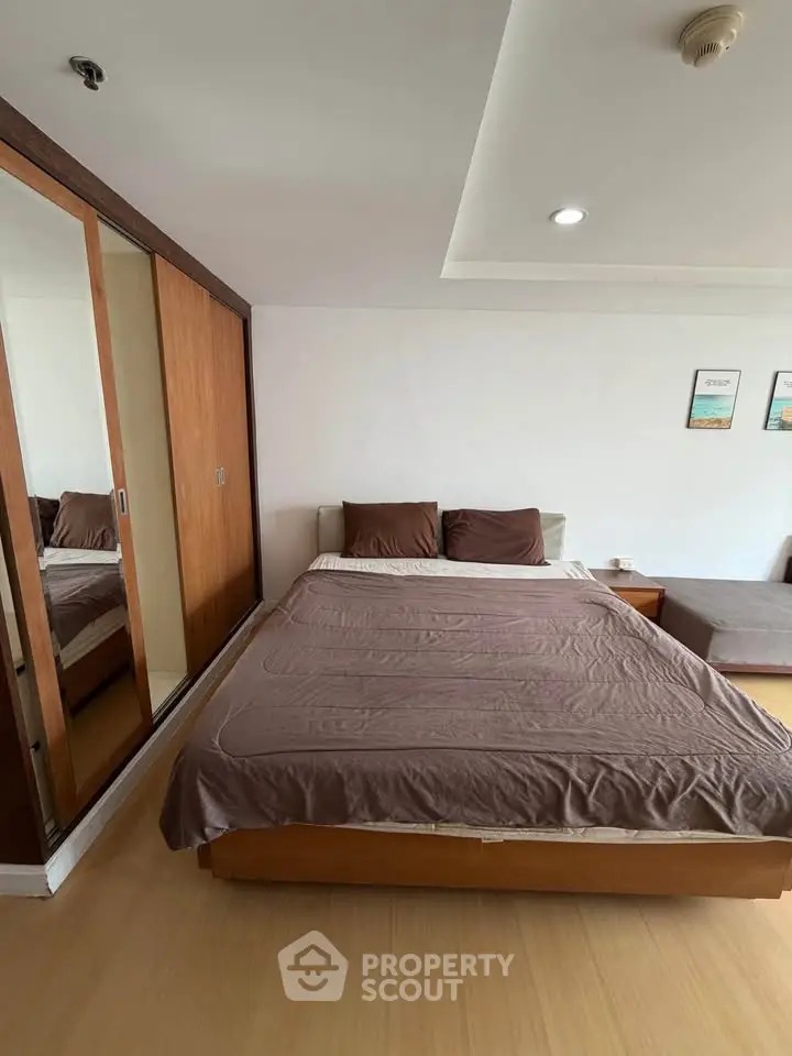 Spacious bedroom with wooden flooring and large mirrored wardrobe in modern apartment.