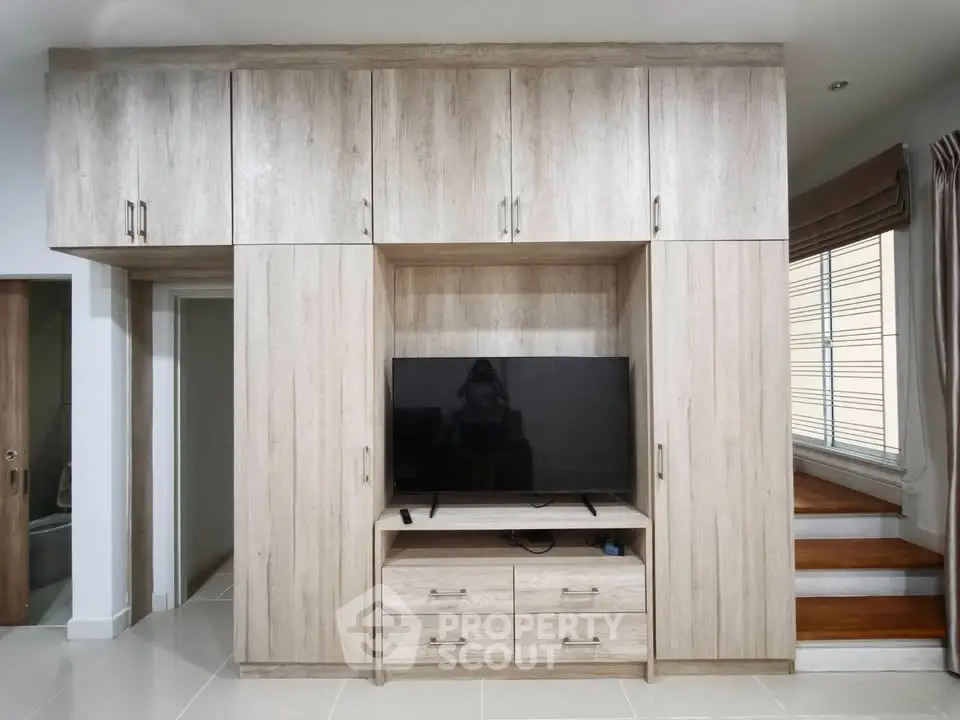 Modern living room with built-in wooden cabinetry and flat-screen TV, showcasing sleek design and functionality.
