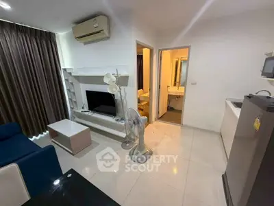 Modern living room with open layout, featuring air conditioning and sleek furniture, adjacent to a compact kitchen.