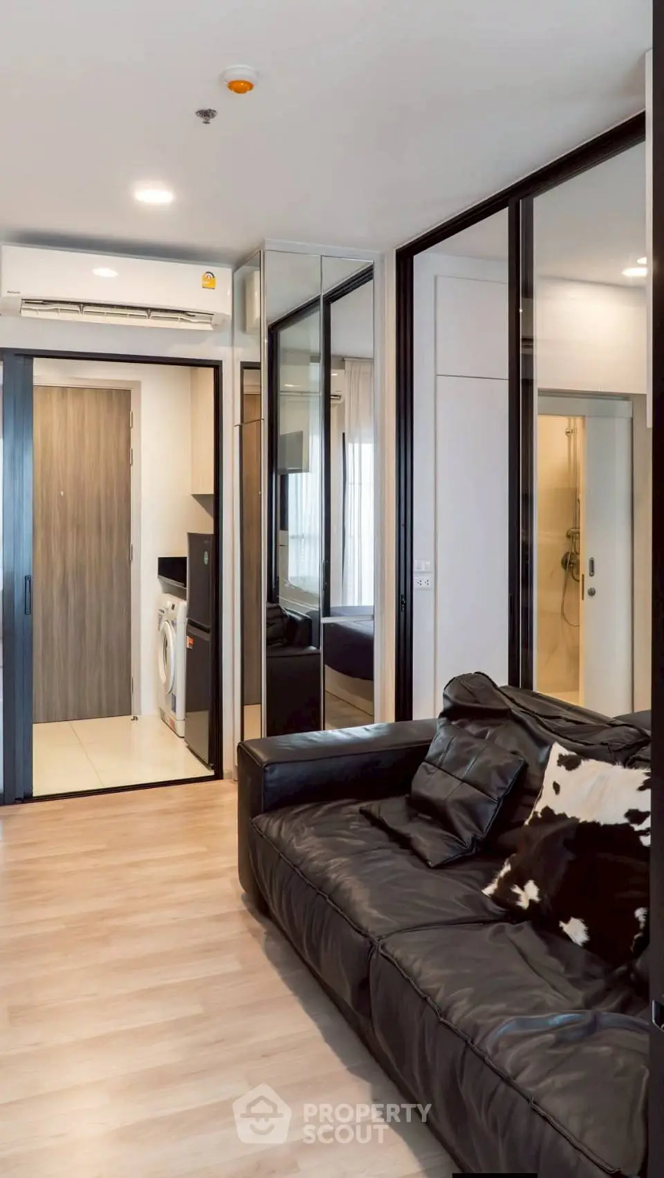 Modern living room with sleek black leather sofa and mirrored walls, featuring a compact laundry area.