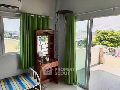 Bright room with balcony access and green curtains, featuring a bed and wooden vanity.