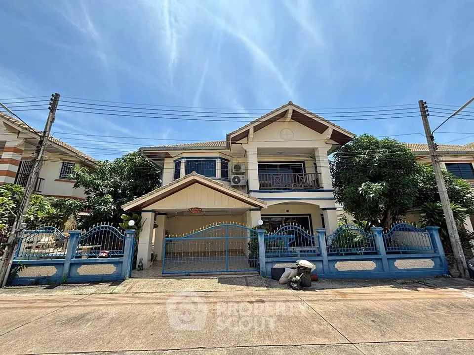 Charming two-story house with blue accents and lush greenery under a clear sky.