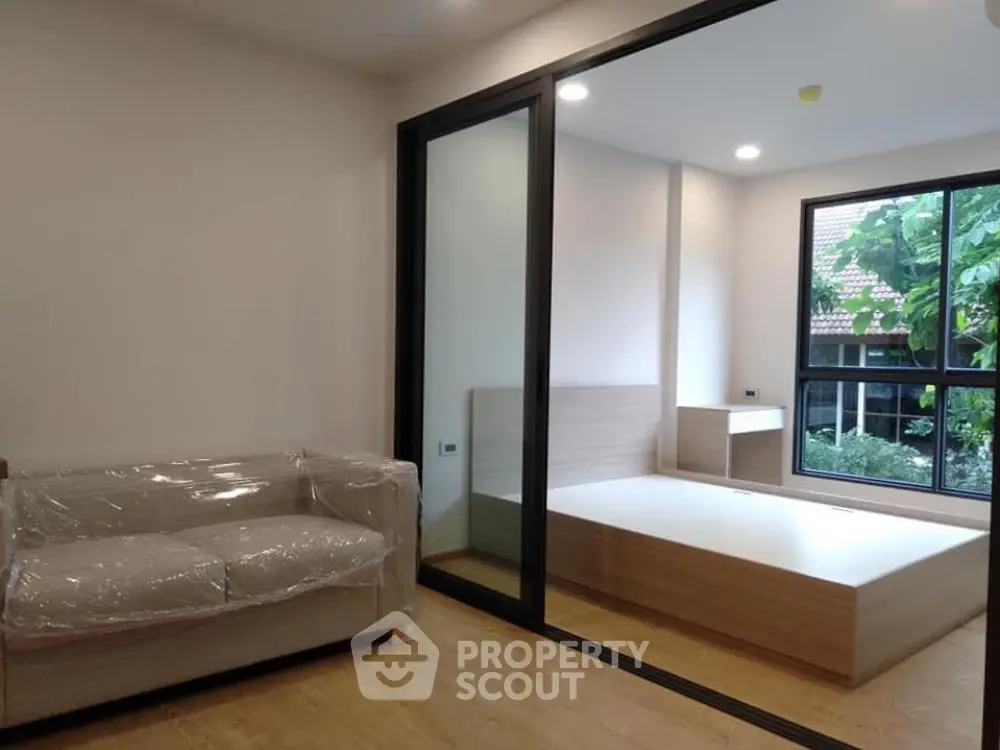 Modern apartment with glass partition, cozy living area, and bright bedroom with garden view.