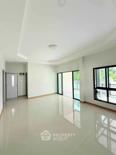 Spacious modern living room with large windows and glossy tiled floors, offering abundant natural light.