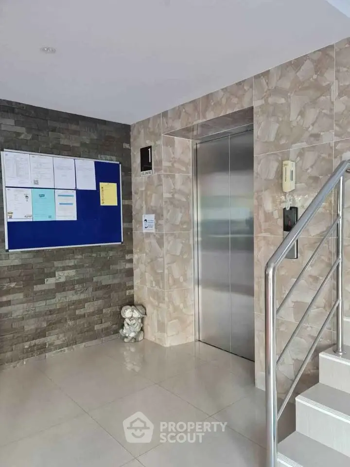 Modern building entrance with elevator and notice board, showcasing sleek design.