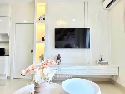 Modern living room with sleek white decor and wall-mounted TV, featuring elegant built-in shelving and ambient lighting.