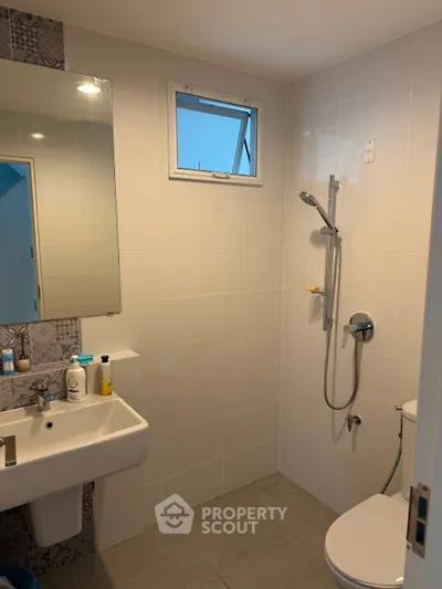 Modern bathroom with sleek fixtures and neutral tiles, featuring a shower and a small window for natural light.