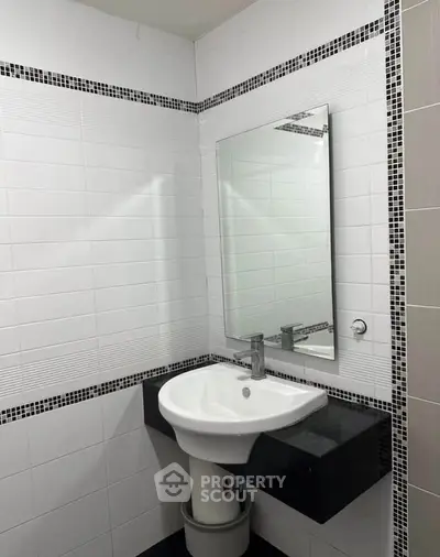 Modern bathroom with sleek sink and mirror, featuring elegant black and white tile design.