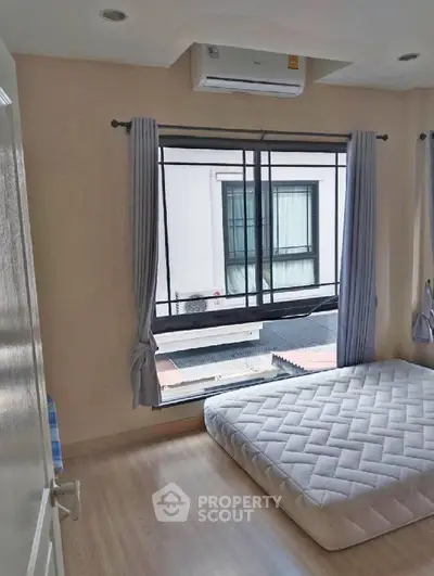 Cozy bedroom with large window and air conditioning unit, perfect for comfortable living.