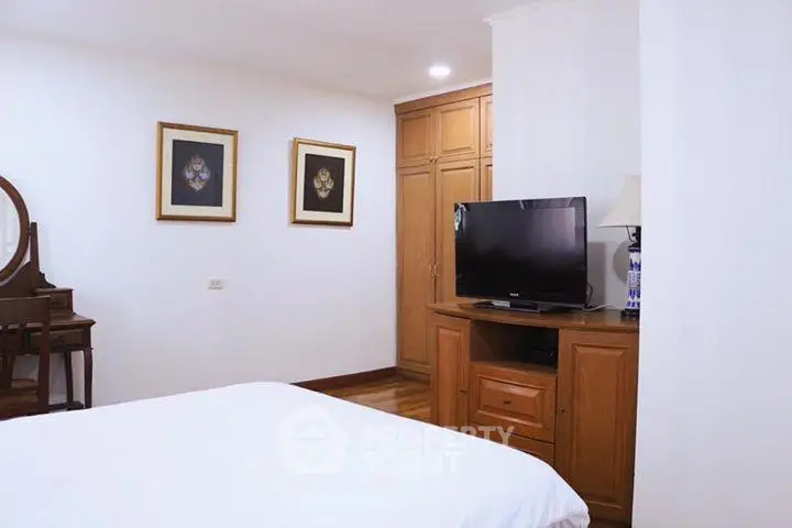 Cozy bedroom with wooden furniture and modern TV setup, perfect for relaxation.
