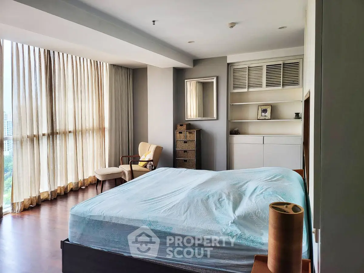 Spacious bedroom with large windows and elegant furnishings in modern apartment.