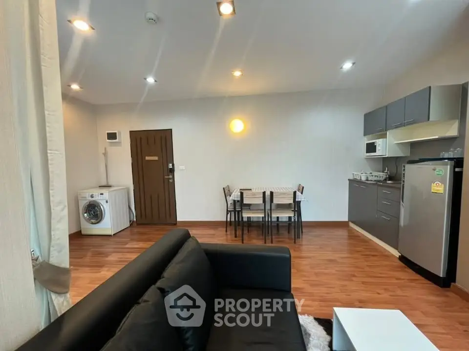 Modern open-plan living room with kitchen and dining area, featuring sleek furniture and wooden flooring.