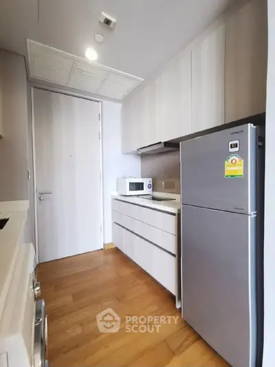 Modern kitchen with sleek cabinets, fridge, and microwave in compact layout.