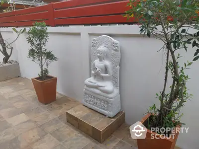 Serene garden corner with a decorative statue and potted plants on tiled flooring.